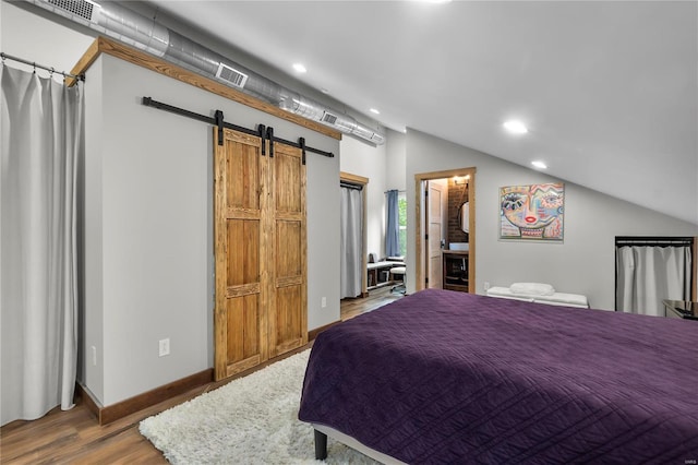 bedroom with hardwood / wood-style floors, vaulted ceiling, and a barn door