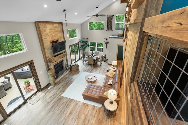 living room featuring ceiling fan, wood-type flooring, a stone fireplace, and high vaulted ceiling