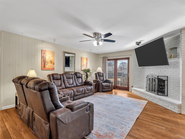 living room featuring wood-type flooring, a brick fireplace, and ceiling fan