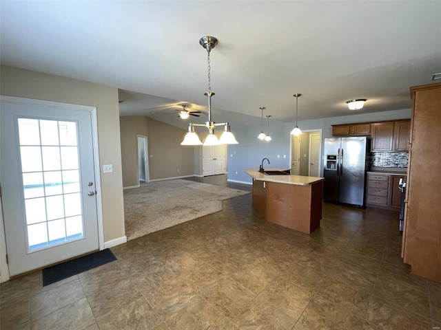 kitchen with pendant lighting, sink, a kitchen island with sink, stainless steel fridge with ice dispenser, and vaulted ceiling