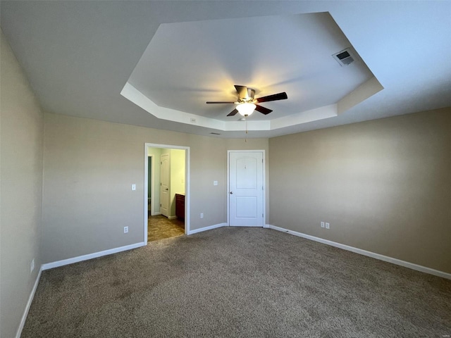 unfurnished bedroom with dark carpet, a tray ceiling, ceiling fan, and ensuite bathroom