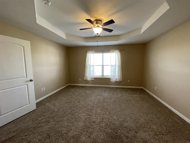 carpeted spare room with a raised ceiling and ceiling fan