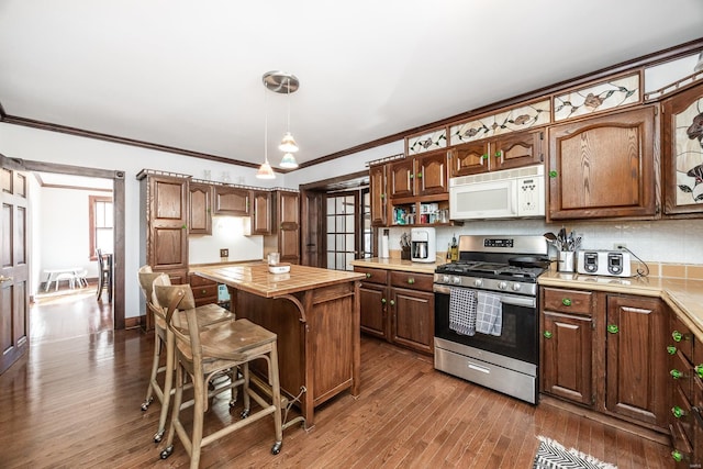 kitchen featuring stainless steel range with gas cooktop, wood-type flooring, hanging light fixtures, ornamental molding, and a center island