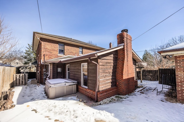 snow covered rear of property with a hot tub