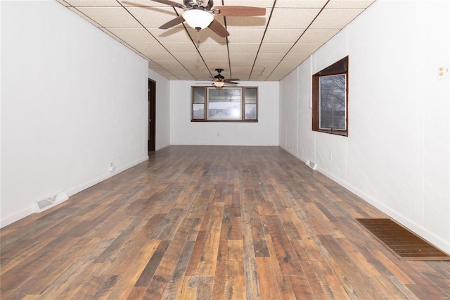 empty room with ceiling fan, dark hardwood / wood-style floors, and a drop ceiling