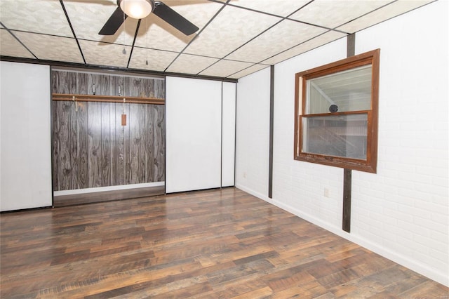 unfurnished room with dark hardwood / wood-style floors, ceiling fan, and brick wall