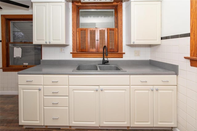 kitchen with dark countertops, tile walls, white cabinets, and a sink