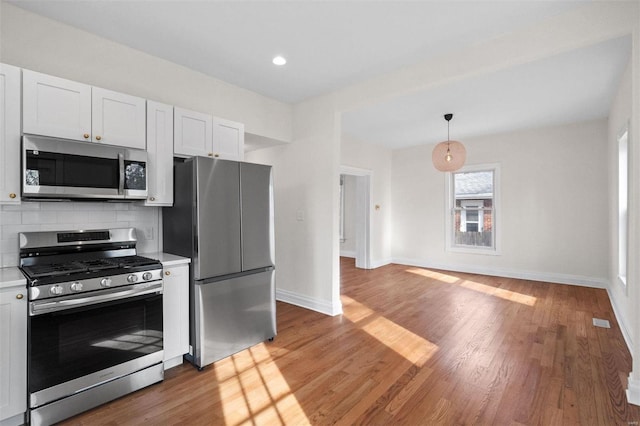 kitchen featuring pendant lighting, hardwood / wood-style flooring, stainless steel appliances, and white cabinets