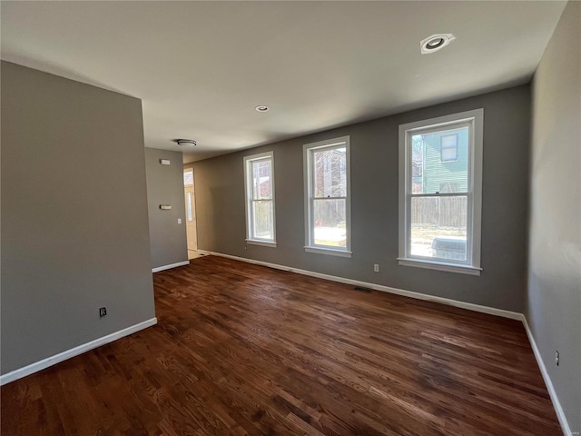 empty room featuring dark wood-style floors, visible vents, and baseboards