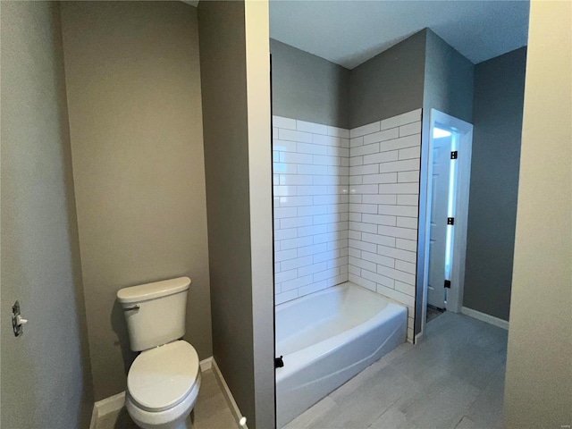 bathroom with bathtub / shower combination, toilet, and baseboards