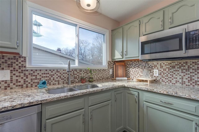 kitchen featuring sink, backsplash, light stone counters, green cabinetry, and stainless steel appliances