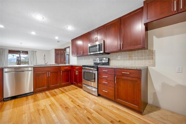 kitchen with light wood-style flooring, a sink, hanging light fixtures, appliances with stainless steel finishes, and decorative backsplash