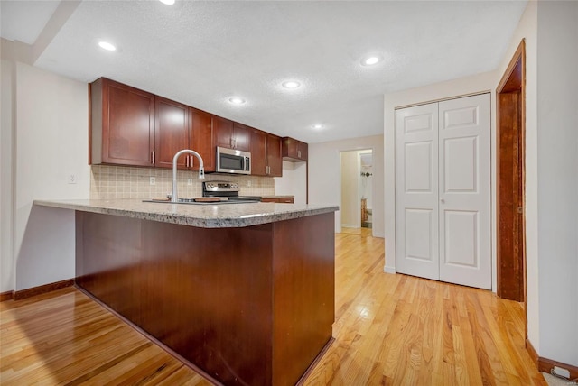 kitchen featuring tasteful backsplash, light wood-style flooring, appliances with stainless steel finishes, a peninsula, and light countertops