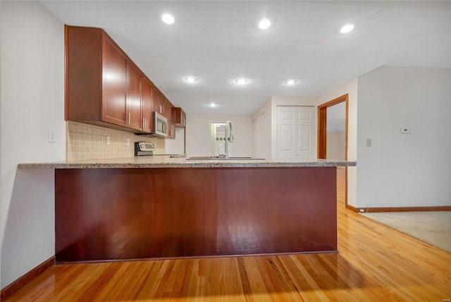 kitchen with light wood finished floors, decorative backsplash, appliances with stainless steel finishes, a peninsula, and a sink