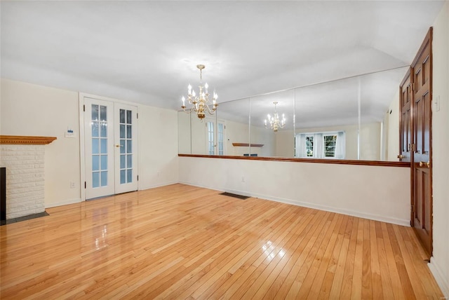 unfurnished living room with light wood finished floors, visible vents, french doors, a fireplace, and a notable chandelier