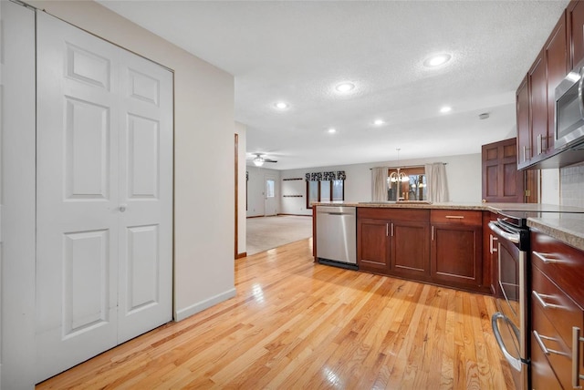 kitchen with decorative light fixtures, stainless steel appliances, light countertops, a sink, and light wood-type flooring