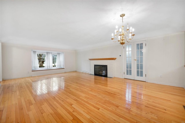 unfurnished living room featuring french doors, a notable chandelier, a fireplace, and light wood finished floors