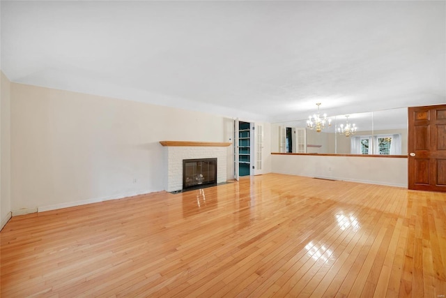 unfurnished living room with light wood-style floors, baseboards, a brick fireplace, and a chandelier