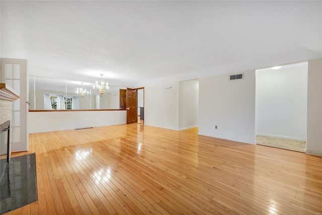 unfurnished living room with a chandelier, a glass covered fireplace, visible vents, and light wood-style flooring