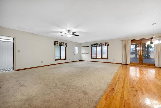 unfurnished living room with ceiling fan with notable chandelier, carpet flooring, and baseboards