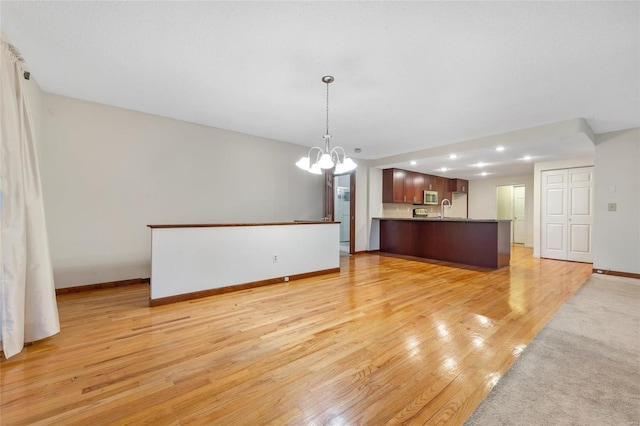 interior space featuring open floor plan, a peninsula, light wood-type flooring, a chandelier, and a sink