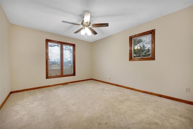 empty room featuring a textured ceiling, carpet floors, ceiling fan, and baseboards