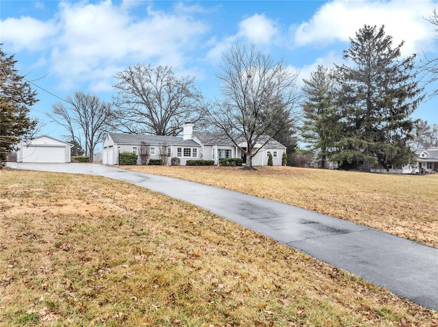 ranch-style house with a garage, a chimney, a front yard, and an outdoor structure