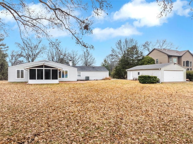 rear view of property with an outbuilding, a detached garage, a sunroom, a yard, and a chimney