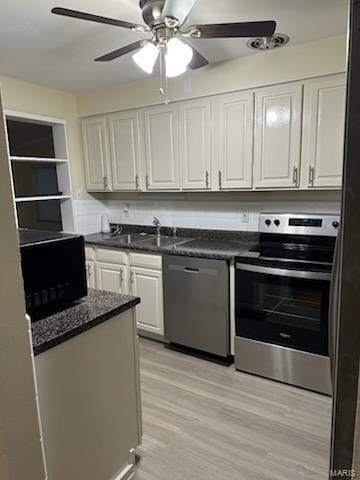 kitchen featuring a sink, light wood-type flooring, dark countertops, appliances with stainless steel finishes, and white cabinets