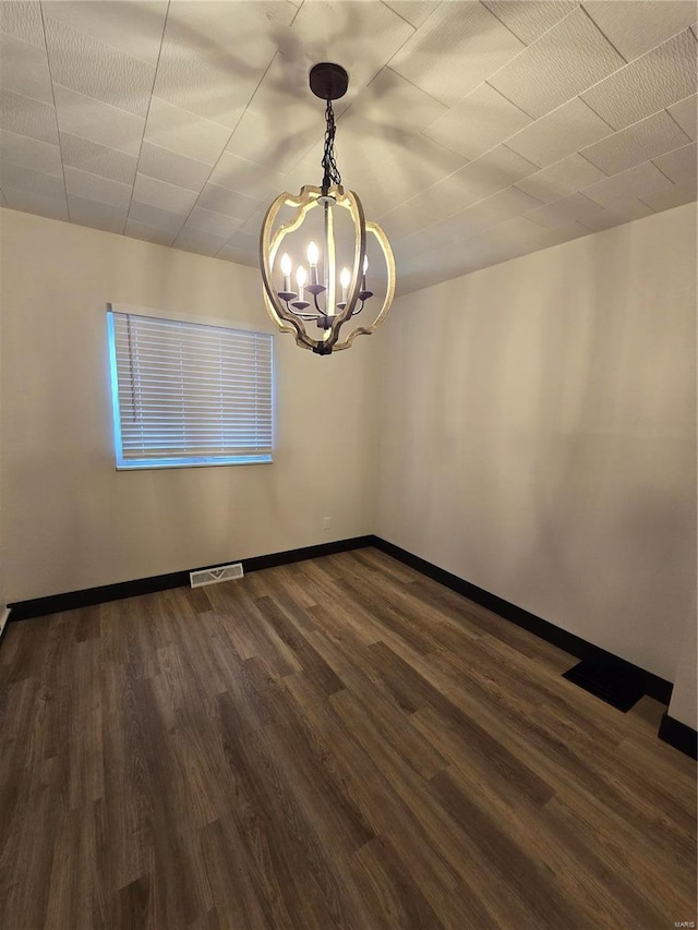 empty room featuring a notable chandelier and dark hardwood / wood-style floors