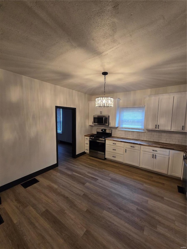 kitchen with dark hardwood / wood-style floors, stainless steel appliances, decorative light fixtures, and white cabinets