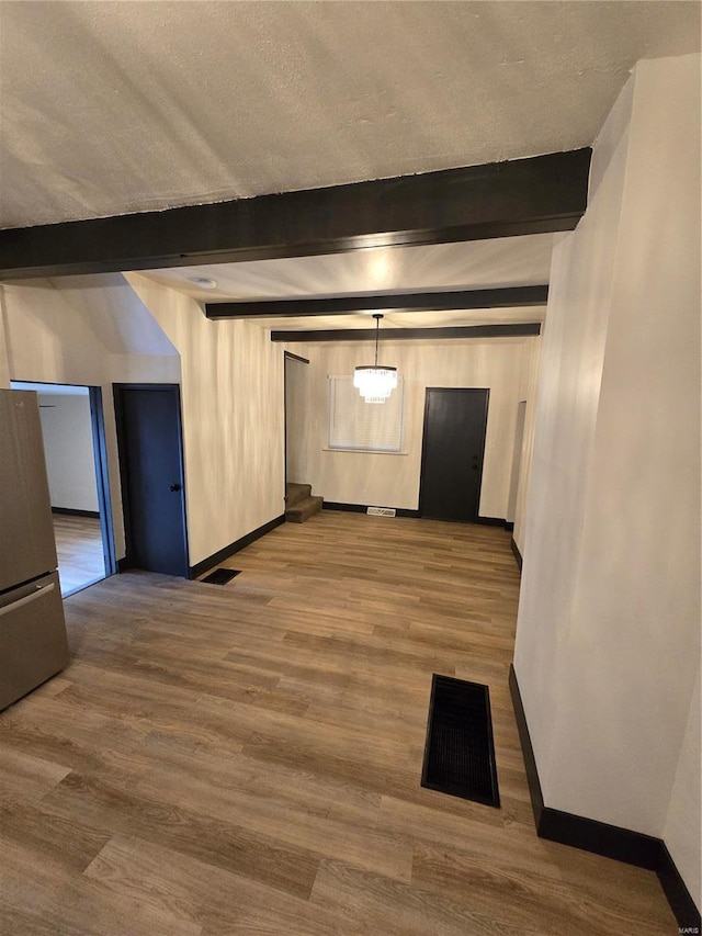 interior space featuring beamed ceiling, wood-type flooring, and a textured ceiling