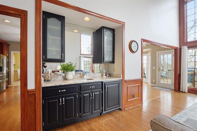 bar with stainless steel fridge with ice dispenser, sink, and light wood-type flooring