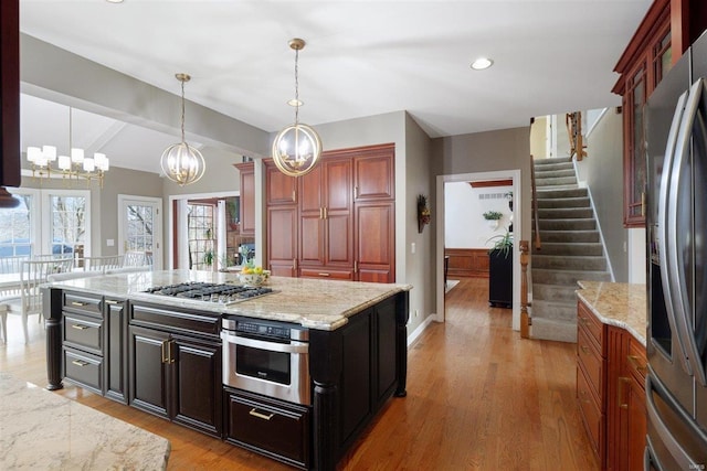 kitchen featuring wood-type flooring, a center island, hanging light fixtures, stainless steel appliances, and light stone countertops