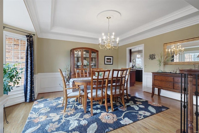 dining room featuring an inviting chandelier, crown molding, a raised ceiling, and light hardwood / wood-style floors