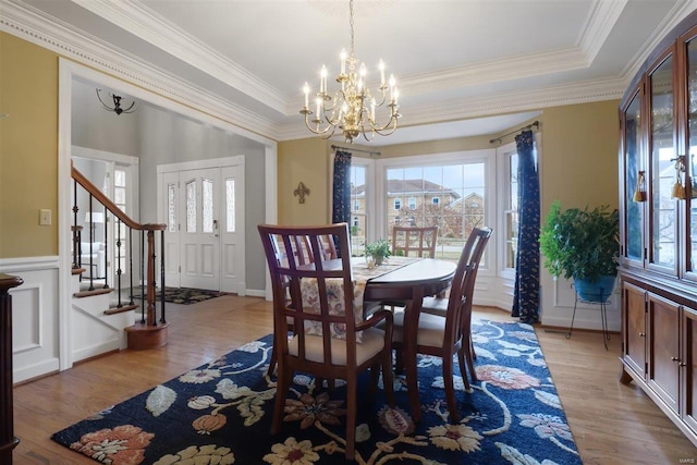 dining space with ornamental molding, a raised ceiling, and light hardwood / wood-style flooring