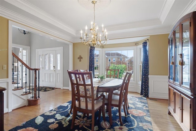 dining room featuring a raised ceiling, ornamental molding, a chandelier, and light hardwood / wood-style flooring