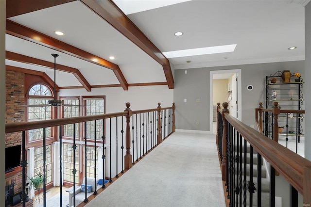 hallway featuring ornamental molding, vaulted ceiling with skylight, and light colored carpet