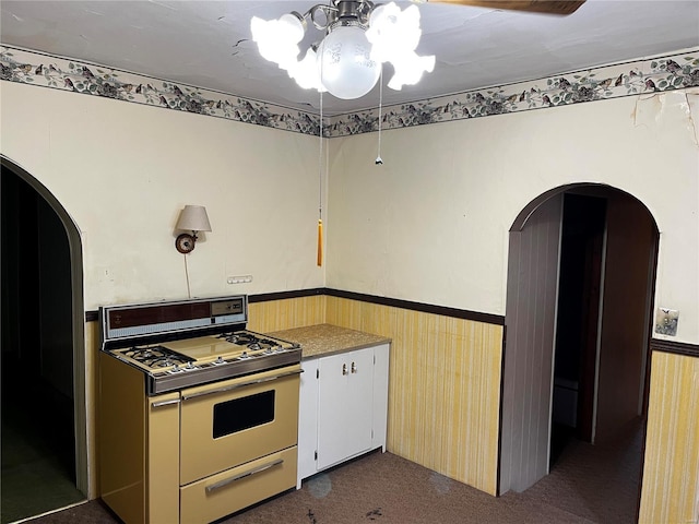 kitchen with gas range, wooden walls, and dark colored carpet