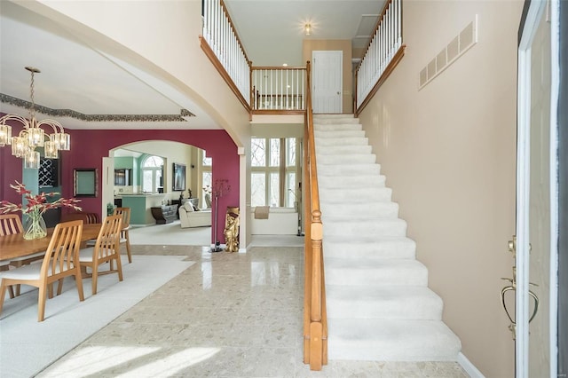 entrance foyer featuring arched walkways, a chandelier, a high ceiling, visible vents, and stairway