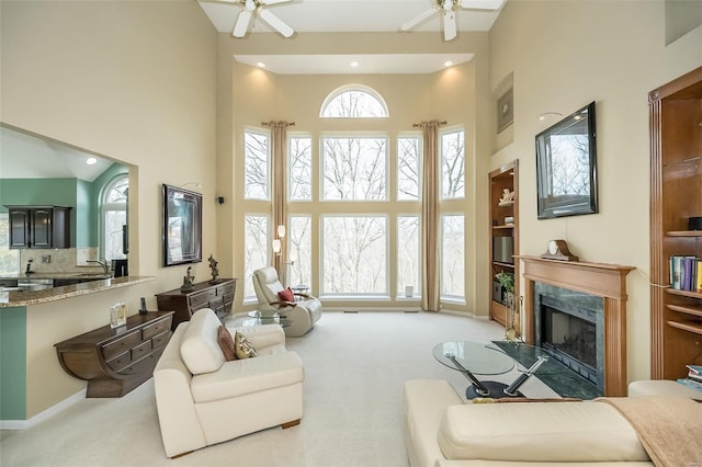 living area with carpet floors, a high end fireplace, a towering ceiling, and a ceiling fan