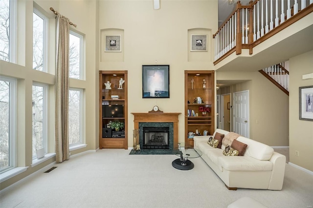 carpeted living room with built in shelves, a high end fireplace, visible vents, and a high ceiling