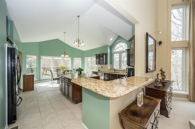 kitchen featuring light stone counters, a kitchen island, a sink, freestanding refrigerator, and an inviting chandelier