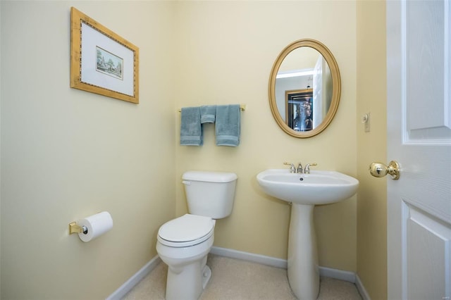 half bath with toilet, baseboards, and a sink