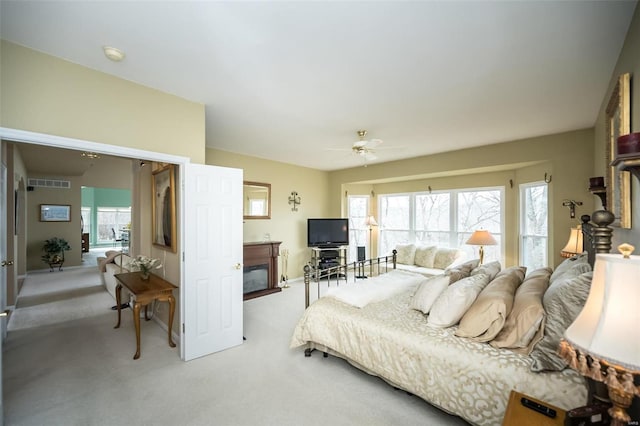 bedroom with ceiling fan, visible vents, a glass covered fireplace, and light colored carpet