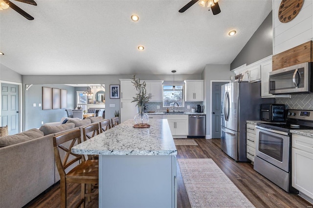 kitchen with a breakfast bar, hanging light fixtures, stainless steel appliances, white cabinets, and a kitchen island