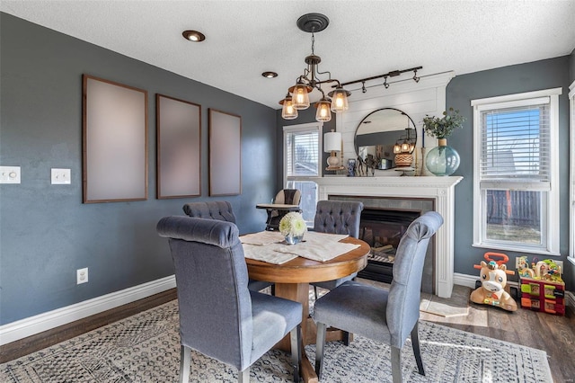 dining space with dark hardwood / wood-style flooring, a notable chandelier, rail lighting, and a textured ceiling