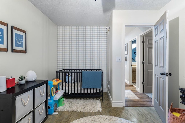 bedroom with a crib, hardwood / wood-style flooring, and a textured ceiling