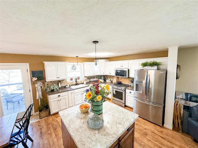 kitchen featuring sink, white cabinetry, a center island, hanging light fixtures, and stainless steel appliances