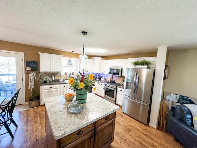 kitchen featuring white cabinetry, a center island, hanging light fixtures, light wood-type flooring, and appliances with stainless steel finishes